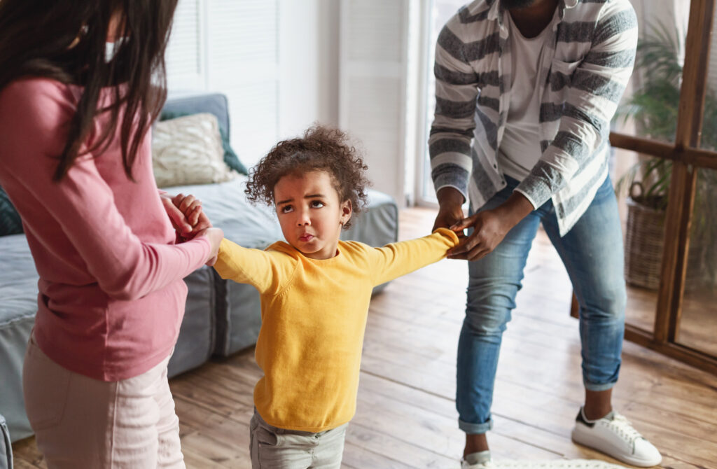 Father and sister pulling on arms of a small girl in a yellow shirt