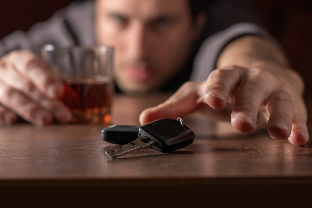 drunk man reaching for his car keys while holding a drink